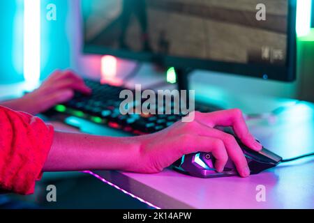 Nahaufnahme der Teenager-Hände mit der Maus während des Videospiels auf neonhellem Hintergrund - Konzept der Unterhaltung, Hobbys und Technologie. Stockfoto