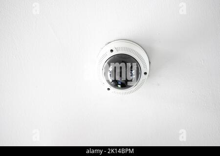 Weiße CCTV-Kamera mit Kuppel aus Acrylglas in der Mitte, die von der Decke hängt. Der Hintergrund ist weißes Studio. Stockfoto