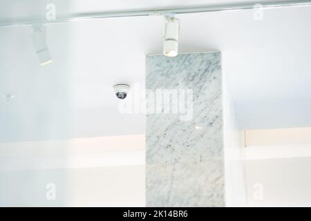 Weiße CCTV-Kamera mit Kuppel aus Acrylglas in der Mitte, die von der Decke hängt. Der Hintergrund ist weißes Studio. Stockfoto