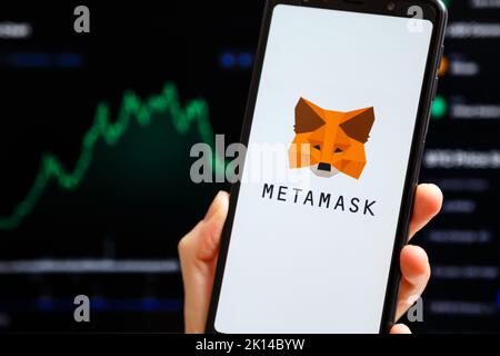 Ukraine, Odessa - Oktober, 9 2021: Hand hält Handy mit MetaMask App läuft auf dem Smartphone-Bildschirm mit Trading Candlestick Chart im Hintergrund. MetaMask ist eine Software-Krypto-Geldbörse Stockfoto
