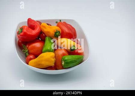Schüssel mit Chilis und Tomaten in einer weißen Schüssel auf weißem Hintergrund. Stockfoto