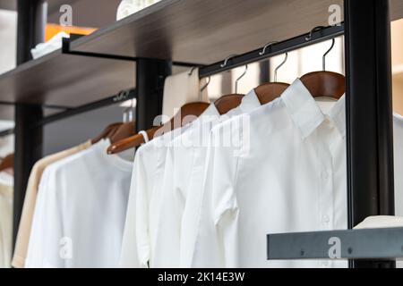 Hemden hängen in einem begehbaren Kleiderschrank mit beigefarbenem und weißem T-Shirt darauf. Stockfoto