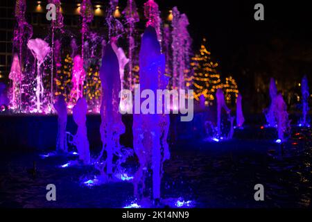 Mehrfarbig beleuchtete Springbrunnenstrahlen im Dunkeln, selektiver Fokus, Bokeh. Festlicher Hintergrund. Stockfoto