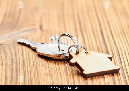 Schmuckkette in Form eines Holzhauses mit den Schlüsseln zur Wohnung auf Holzhintergrund Stockfoto