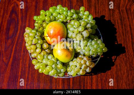 Grüne Trauben und Äpfel in einer Obstschale auf einem Holztisch, Draufsicht. Frische Früchte, Stillleben. Stockfoto