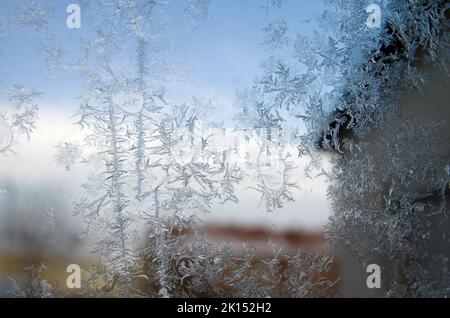 Gefrorene Eiskristalle auf einem Stadtfenster im eisigen Londoner Winter bilden kristalline Formen mit verschwommenen Gebäuden im Hintergrund Stockfoto