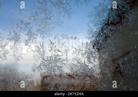 Gefrorene Eiskristalle auf einem Stadtfenster im eisigen Londoner Winter bilden kristalline Formen mit verschwommenen Gebäuden im Hintergrund Stockfoto