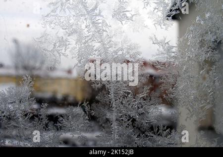 Gefrorene Eiskristalle auf einem Stadtfenster im eisigen Londoner Winter bilden kristalline Formen mit verschwommenen Gebäuden im Hintergrund Stockfoto