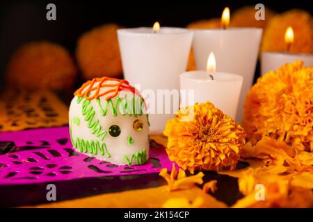 Zuckerschädel mit Kerze, Crepasuchil-Blüten oder Ringelblume und Papel Picado. Dekoration traditionell in Altären für die Feier des Tages verwendet Stockfoto