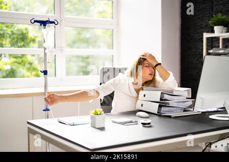 Intravenöse Tropfentherapie im Büro. Kranke Frau Arbeitslast Stockfoto