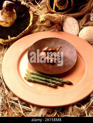 Honigpilz oder Armillaria mellea auf einer Kupferplatte entlang des Spargels auf einer Terrakotta-Platte in einem rustikalen Stilleben mit Portobello-Pilzen Stockfoto