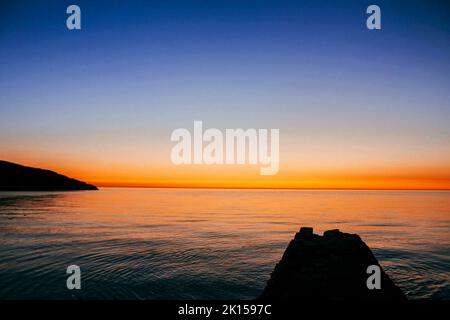 Schöner orangefarbener Sonnenuntergang über dem Meer am Trefor Beach, Wales im Sommer Stockfoto