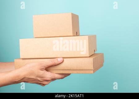 Stapel von Kartons in weiblichen Händen. Leere braune Paketboxen auf hellblauem Hintergrund. Modell. Verpackung, Einkaufen, kostenloser Versand, Lieferung Stockfoto