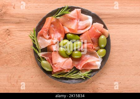 Charcuterie-Teller mit Proscuitto serviert mit Oliven auf Holztisch Hintergrund. Traditionelle italienische Antipasti. Selektiver Fokus Stockfoto