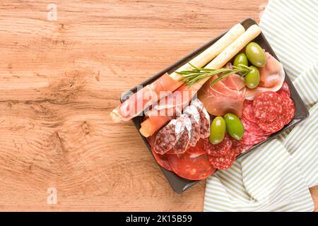 Traditionelle italienische Küche - Antipasti. Wurstplatte mit Wurstsorten - Salami, bresaola, Proscuitto, serviert mit Oliven und Grissini auf Woo Stockfoto