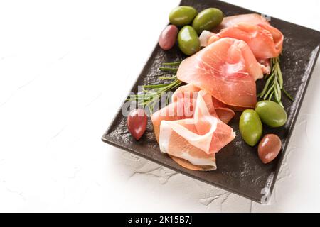 Charcuterie-Teller mit Proscuitto serviert mit Oliven auf weißem Tischhintergrund mit Kopierplatz. Traditionelle italienische Antipasti. Selektiver Fokus Stockfoto