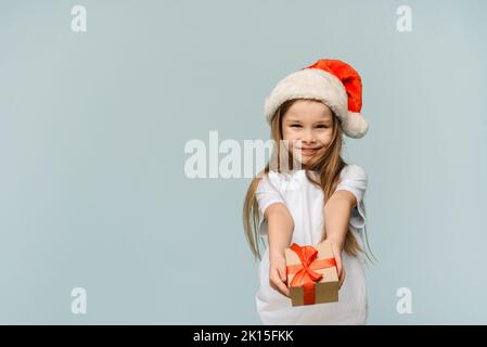 Lustige niedliche Mädchen in einem weihnachtsmann Hut gibt ein Geschenk auf einem blauen Hintergrund mit Kopierraum. Konzept von weihnachten und Neujahr Stockfoto