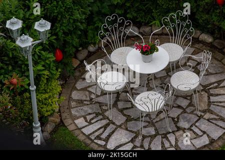 Luftbild von Tisch und Stühlen im Freien aus Schmiedeeisen auf Stein Terrasse im Garten mit Rasen und großen Pflanzen herum, Garten- und Landschaftsbau Home de Stockfoto