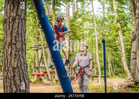 Mutter und Sohn klettern in extreme Straße Trolley Zipline im Wald auf Karabiner Sicherheitslink auf Baum zu Baum top Seil Abenteuerpark. Familienwochenende Stockfoto