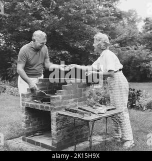 Ein älteres Paar genießt die Gesellschaft des anderen, während sie draußen in ihrem Hinterhof kochen. Stockfoto