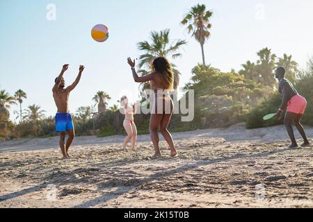 Verschiedene Männer und Frauen werfen Ball und spielen Beachtennis, während sie am Sommerwochenende gemeinsam am Sandstrand verbringen Stockfoto