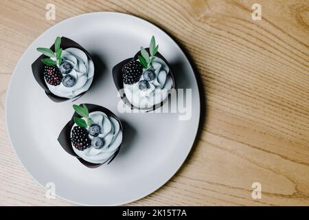 Drei Schokoladen-Cupcakes mit Beeren auf einem weißen Teller. Blick von oben. Stockfoto