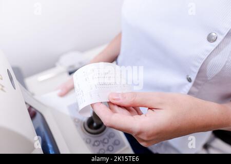 Von oben der Ernte nicht erkennbar weibliche okulistische Lesung Rezept für Brillen, während in der Nähe von Autorefraktor in der modernen Klinik Stockfoto
