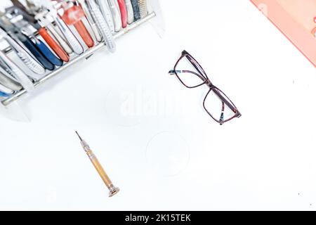 Draufsicht auf Brillen und Schraubendreher, die auf einem weißen Tisch in der Nähe von verschiedenen Werkzeugen im modernen optischen Büro platziert sind Stockfoto