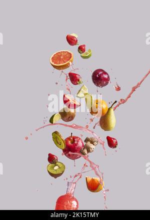 Ein paar verschiedene frische Früchte und Ingwer fallen in eine Glasflasche mit gesundem Saft vor grauem Hintergrund Stockfoto