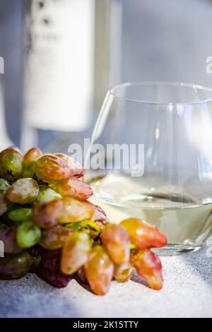 Weißer trockener Wein im Glas und reife Trauben auf grauem Hintergrund Stockfoto