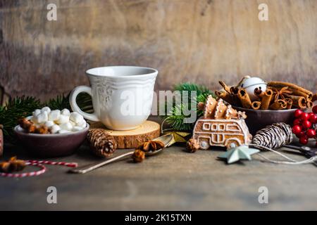 Becher mit Heißgetränk und Mini-Marschmalchen mit Gewürzen auf dem Hintergrund mit weihnachtsdekorationen Stockfoto