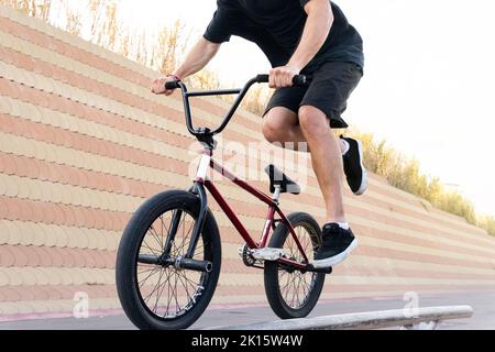 Cropped unkenntlich fokussierten Mann in schwarzem T-Shirt und Shorts in der Nähe Betonwand auf BMX Fahrrad, während Tricks auf der Bahn City Straße Stockfoto