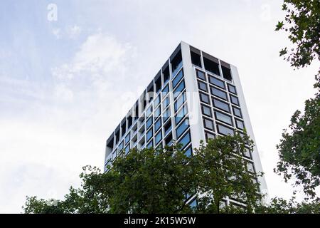 Von unten graue Fassade des modernen mehrstöckigen Hauses mit zahlreichen Fenstern, die sich am sonnigen Sommertag in der Stadt gegen den bewölkten Himmel befinden Stockfoto