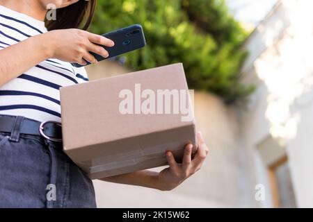 Von unten Ernte unkenntlich weibliche Kurierin legerer Kleidung Foto von Karton auf dem Smartphone während der Lieferung Paket Stockfoto