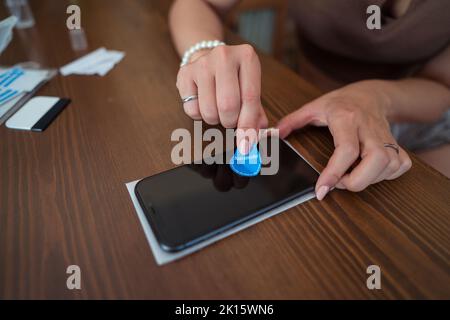 Von oben anonyme Frau mit Staubabsorber zu reinigen Bildschirm des Mobiltelefons, bevor Schutzglas auf dem Tisch kleben Stockfoto