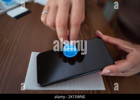 Von oben anonyme Frau mit Staubabsorber zu reinigen Bildschirm des Mobiltelefons, bevor Schutzglas auf dem Tisch kleben Stockfoto