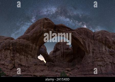 Atemberaubender Blick auf den Arid Arches National Park durch die raue Double Arch Formation gegen die glühende Milchstraße am Nachthimmel in Utah, USA Stockfoto