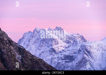 Scharfe Berggipfel teilweise mit Schnee bedeckt unter malerischem rosafarbenem Himmel bei Einbruch der Dunkelheit im Winter Stockfoto