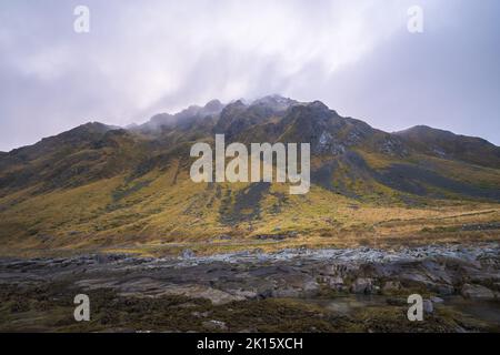Schneller Strom von sauberem Wasser, der zwischen Felsen in der Bergkette gegen den bewölkten Himmel in Lofoten, Norwegen, fließt Stockfoto