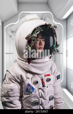 Asiatische Frau im Astronaut-Kostüm und Helm mit grüner Weinrebe, die während der Weltraummission im Raumschiff wegschaut Stockfoto