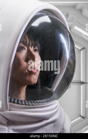 Asiatische Frau in Astronaut-Kostüm und Helm wegschauen während der Weltraummission im Raumschiff Stockfoto