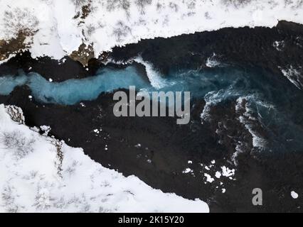 Luftaufnahme der schäumenden Meereswellen, die am kalten Wintertag in Island an der rauen, mit Schnee bedeckten Felsküste plantschen Stockfoto