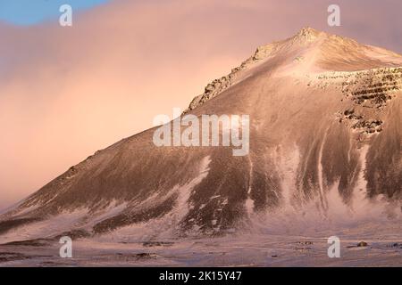 Schneebedeckter Berggipfel am wolkigen Sonnenaufgangshimmel am kalten Wintermorgen in Island Stockfoto