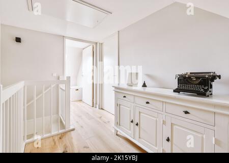 Innenraum des modernen Korridors mit weißer Treppe und Türen in der Nähe von Schrank mit Dekorationen tagsüber im Haus Stockfoto