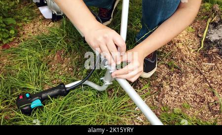 Ein Mann montiert den Griff des Saitentrimmers im Garten. Stockfoto