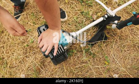 Gärtner Mann Hand Start Gas Rasen Trimmer. Hände eines professionellen Rasenmähers. Stockfoto