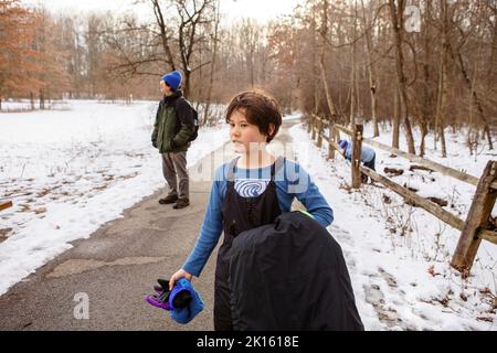 Ein Junge in Winterkleidung geht mit der Familie auf dem Weg durch den Wald Stockfoto