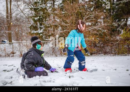 Ein Junge bringt seiner kleinen Schwester das Snowboarden im Winter bei Stockfoto