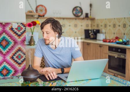 Diffusor für ätherisches Öl auf dem Tisch dampft, während der Mann einen Laptop benutzt Stockfoto