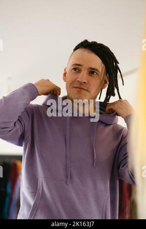 Junger Mann, der in Spiegel schaut, wenn er seine neuen Dreadlocks bedenkt. Schöner Kerl preening vor dem Spiegel im Friseursalon Stockfoto